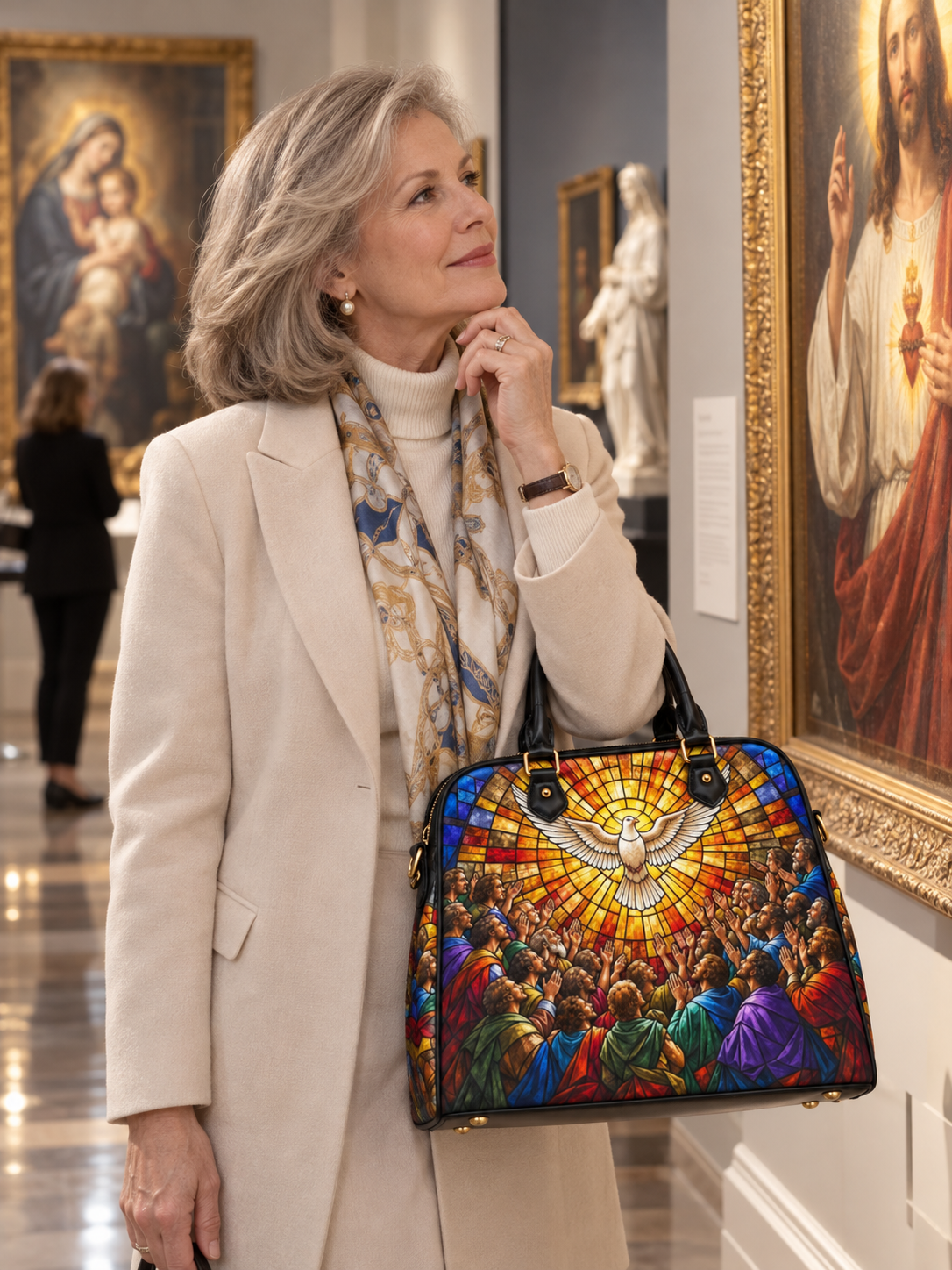 A woman in a cream blazer and patterned scarf carries a structured handbag with a colorful stained-glass-style religious scene featuring a dove and figures in red, blue, green, and gold tones, set against an art gallery background.