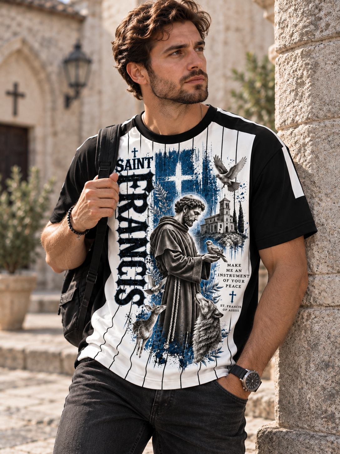 A short-sleeve athletic-style T-shirt with a black and white pinstripe design, featuring a large graphic print of Saint Francis on the front with blue watercolor-style background details, text reading 'SAINT FRANCIS,' and religious imagery including a cross, dove, and building.
