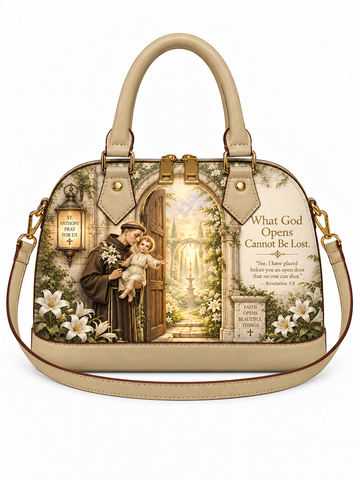 A beige leather handbag with a detailed religious graphic print on the front, featuring a saint holding a child at an open cathedral door, white lilies, and a Bible verse. The bag has double top handles and a matching shoulder strap, shown against a plain white background.