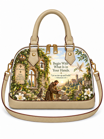 A structured dome-shaped handbag with beige leather handles and shoulder strap, featuring a detailed scenic print of Saint Francis of Assisi tending sheep in a garden with a cathedral and the text 'Begin With What Is in Your Hands.' on the front, shown on a plain white background.