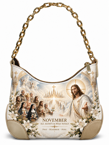 A hobo-style shoulder bag with a gold chain strap, featuring a large religious graphic print on the front. The print depicts Jesus Christ, saints, a basilica, and the text 'NOVEMBER ALL SAINTS & HOLY SOULS'.