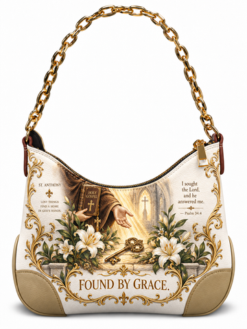 A hobo-style shoulder bag with a gold chain strap, featuring a detailed religious graphic on the front. The design includes a saint, a Bible, white lilies, a golden key, and scripture text, with the phrase 'FOUND BY GRACE.