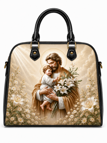 A structured black handbag with dual top handles and gold-tone hardware, featuring a large printed religious artwork on the front. The print shows a bearded man in brown robes holding a child, surrounded by white lilies and small flowers against a warm cream background with light rays.