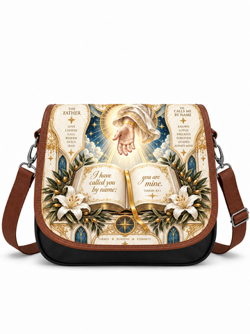 A messenger-style shoulder bag with a brown leather trim and black base, featuring a large printed religious illustration on the front. The artwork shows a radiant hand, an open Bible with the words 'I have called you by name; you are mine,' lilies, and religious text panels.
