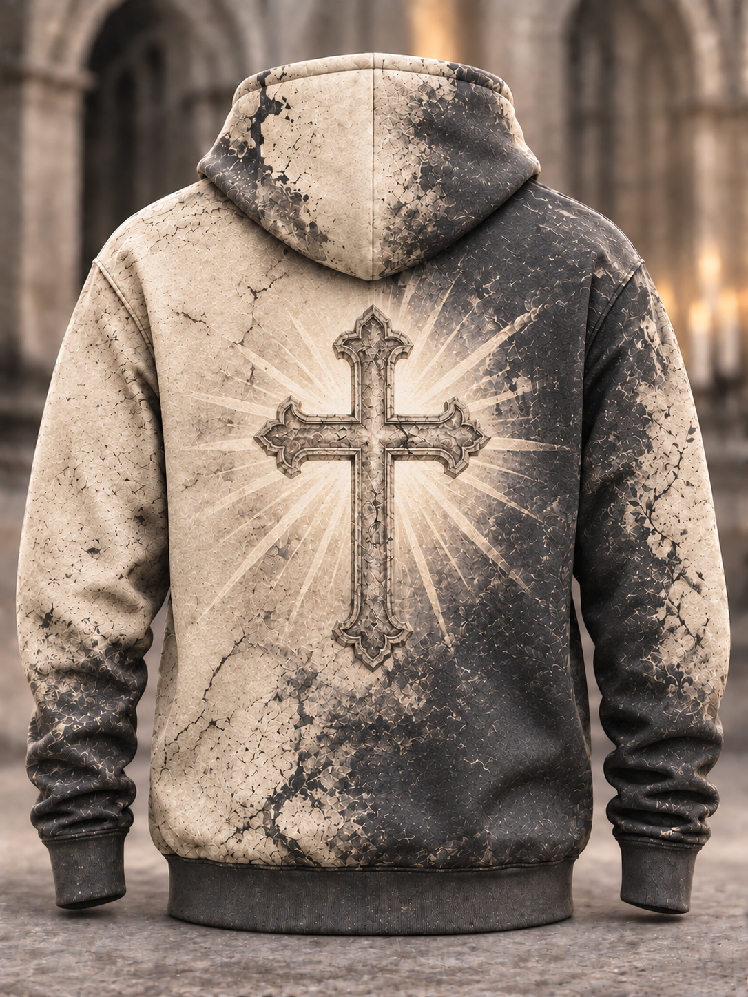 Back view of a hooded sweatshirt with a distressed, washed-out design in beige and dark gray/black, featuring a large cross with a radiant sunburst graphic on the back. The hoodie is shown against a blurred stone cathedral background.