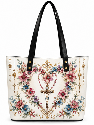 A white tote bag with black faux-leather shoulder straps, decorated with a detailed religious floral print featuring a central crucifix, rosary beads, pink and blue flowers, and gold ornamental details.
