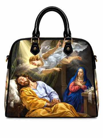 A structured black handbag with dual top handles, featuring a large printed religious painting on the front. The artwork depicts Jesus sleeping in a bed, Mary in blue and red robes at a table, and an angel flying in the sky.