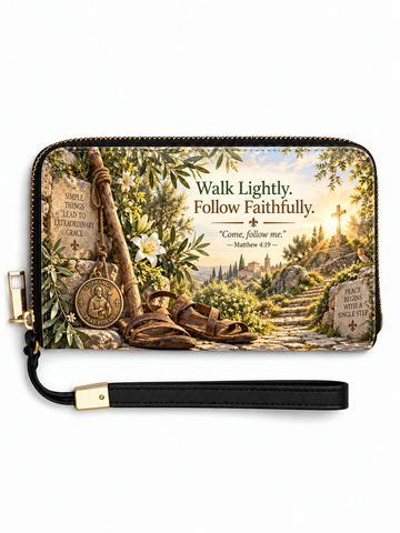 A zip-around wallet with a wrist strap, featuring a scenic religious illustration of a path toward a cross, sandals, a medal, and text reading 'Walk Lightly. Follow Faithfully.