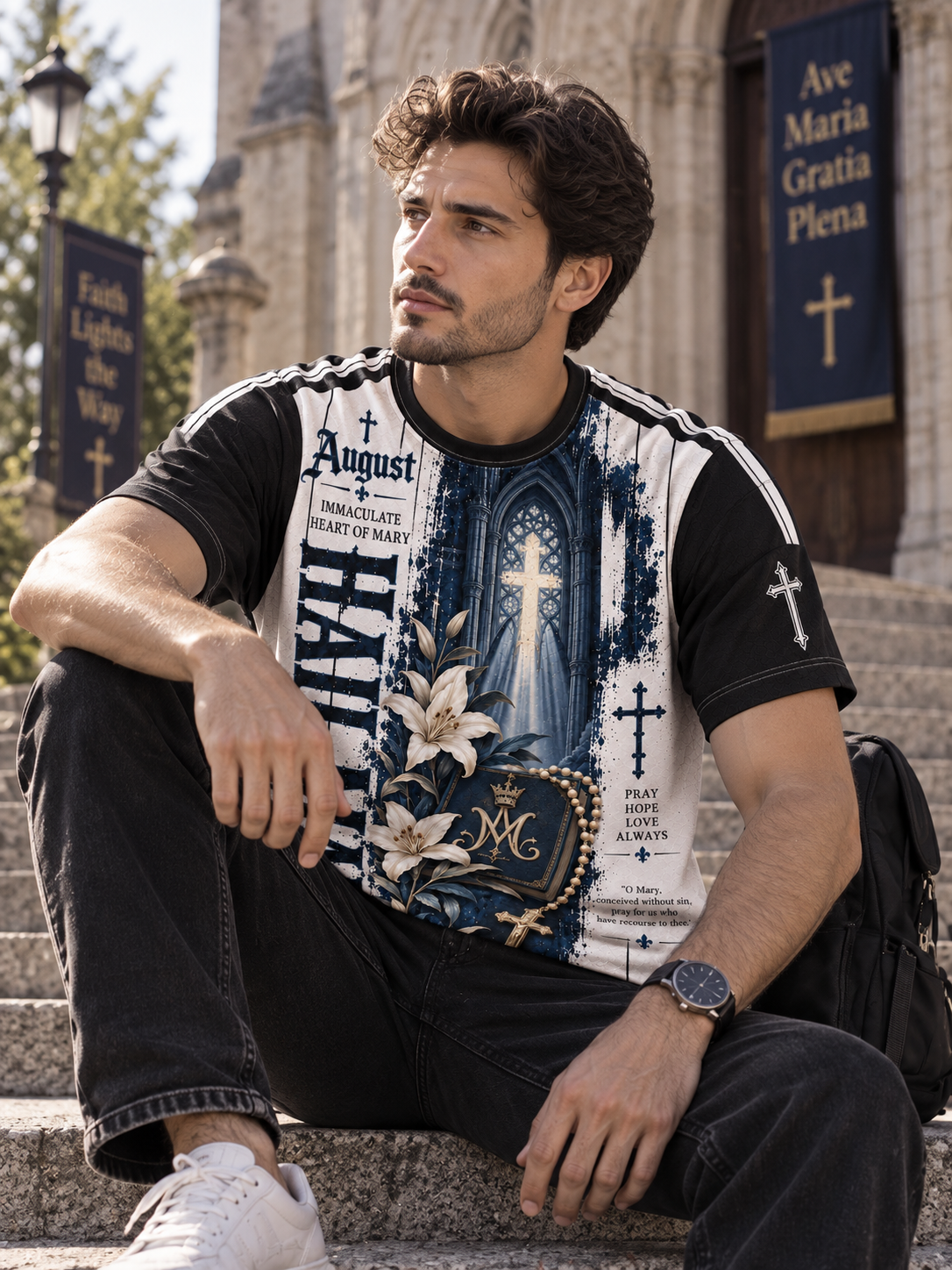 A man sits on stone steps in front of a church, wearing a black and white graphic t-shirt with religious illustrations and text, dark jeans, and white sneakers.