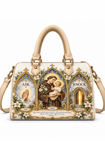 A structured cream-colored handbag with gold-tone hardware and dual top handles, featuring a large, detailed religious graphic print on the front. The print depicts Saint Francis of Assisi holding the infant Jesus, surrounded by white flowers and gold-arched panels with the words 'ASK', 'MARK', and 'KNOCK'.