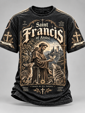 A black short-sleeve graphic t-shirt featuring a detailed vintage-style illustration of Saint Francis of Assisi, with deer, a wolf, a castle, and ornate gold-toned text on a gray studio background.