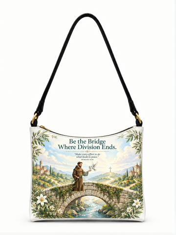 A white shoulder bag with a black strap and gold-tone hardware, featuring a printed graphic of a saint standing on a stone bridge over a river, surrounded by white lilies and green foliage. The text above reads, 'Be the Bridge Where Division Ends.
