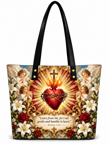 A black shoulder tote bag featuring a highly detailed, colorful graphic print of the Sacred Heart of Jesus, flanked by cherubs, lilies, and roses, with a Bible verse printed below.