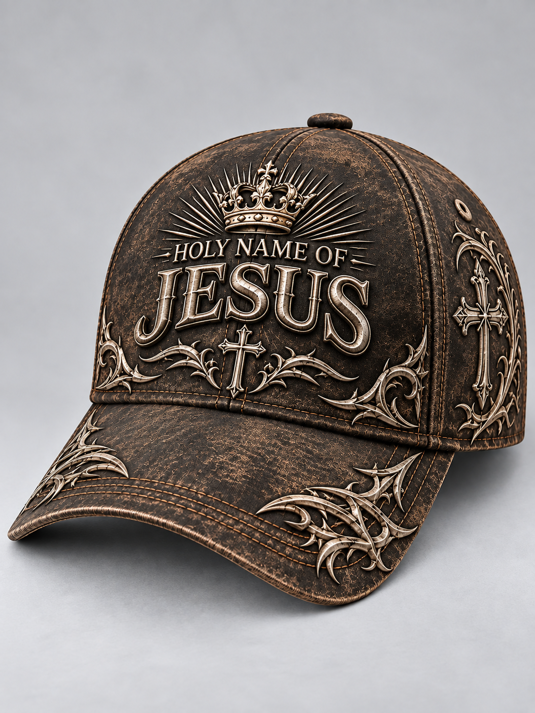 A distressed brown baseball cap featuring raised metallic-style embroidery that reads 'HOLY NAME OF JESUS' with a crown and ornate cross motifs on the front and brim, shown on a light gray studio background.