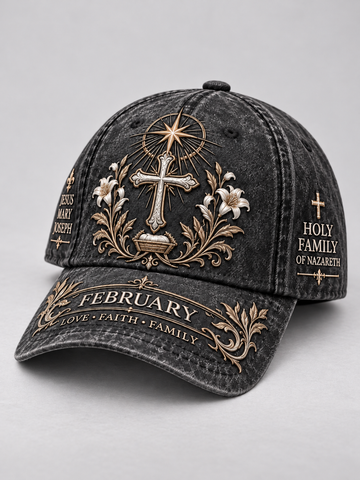 A dark gray washed baseball cap with ornate gold and white embroidered religious designs, including a cross, floral elements, and text reading 'February Love • Faith • Family' on the brim and 'Holy Family of Nazareth' on the side panels.