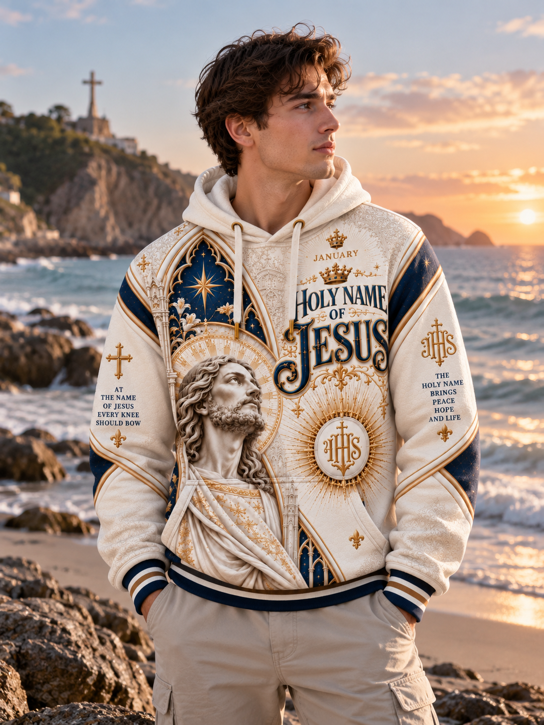 A hooded sweatshirt with a large religious graphic print featuring a robed figure, ornate arch details, and the text 'Holy Name of Jesus' in navy and gold on an off-white background.