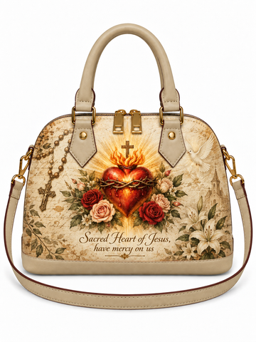 A beige leather handbag with a detailed 'Sacred Heart of Jesus' graphic print on the front, featuring a red flaming heart, roses, lilies, a rosary, and the text 'Sacred Heart of Jesus, have mercy on us'.